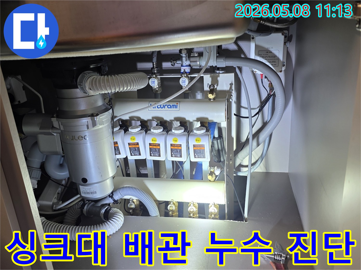 싱크대 아래-복잡하게 얽힌 배관과-정수기 시스템-음식물처리기 사이에서-누수 흔적을-전문가가 면밀히 살피는 모습입니다
