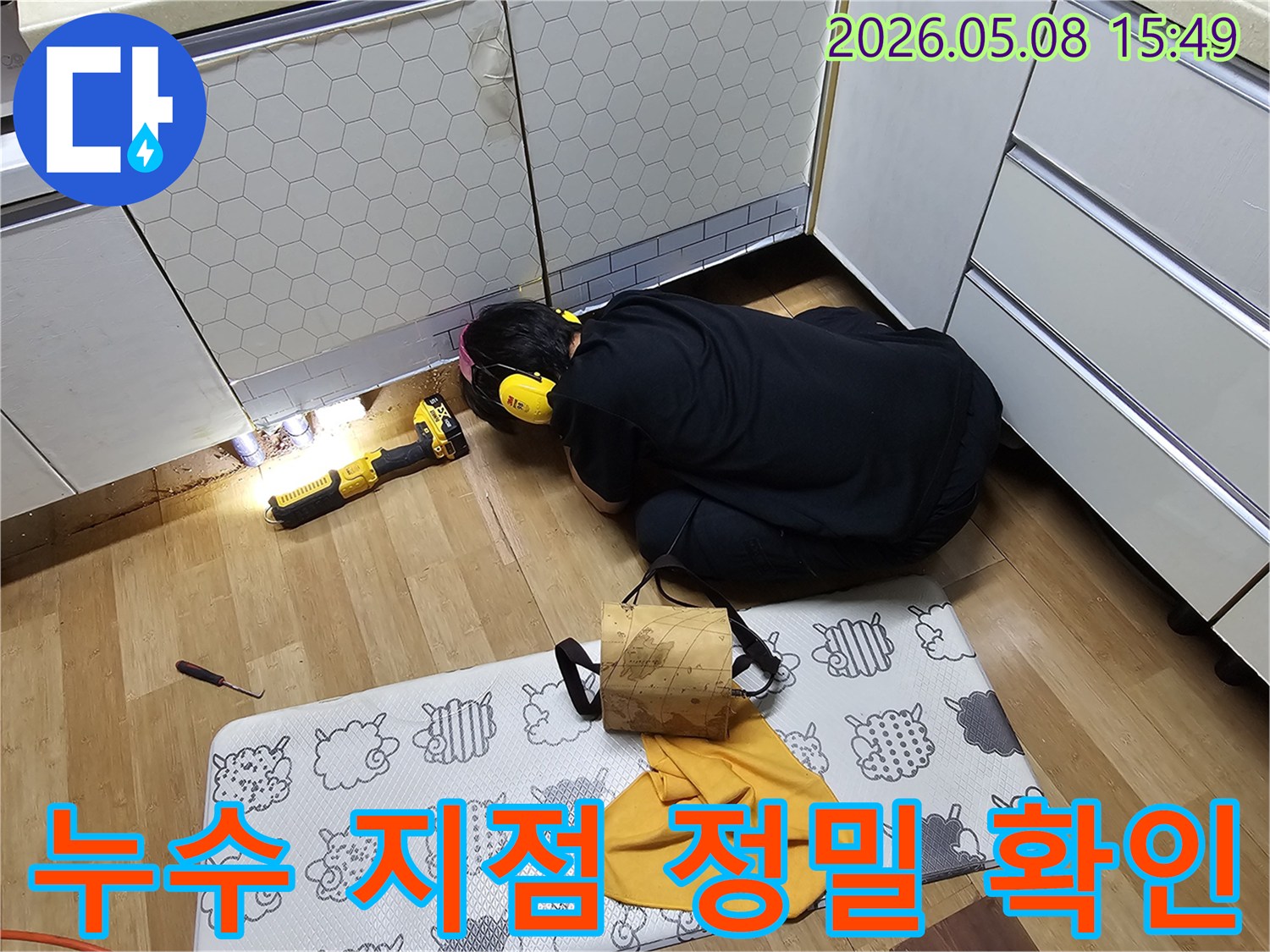 전문 기술자가-주방 바닥의 누수 지점을-밝은 손전등으로-세밀하게 조사하고 있습니다.