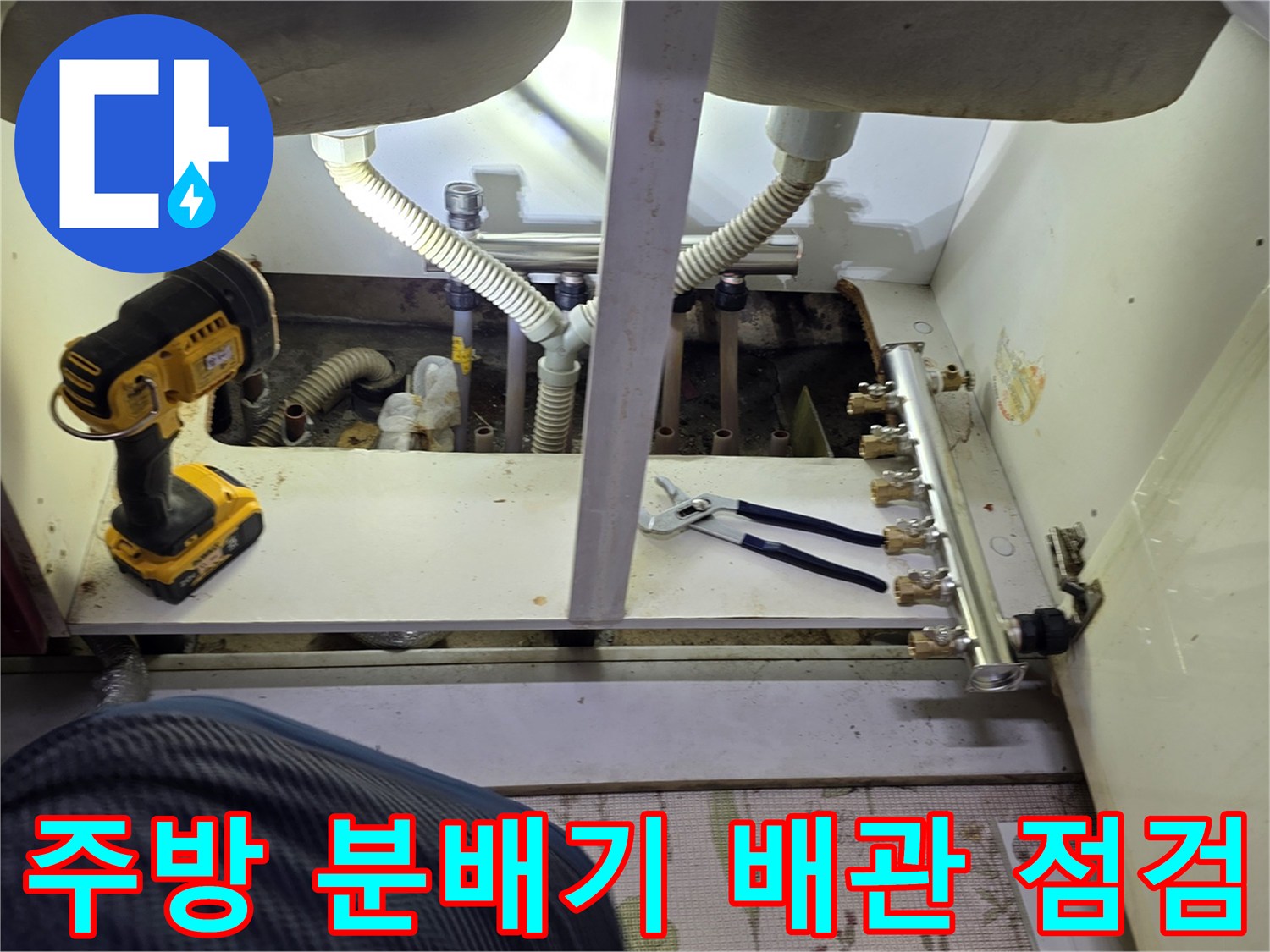 싱크대 하단 공간에서 보일러 분배기와 연결된 배관들을 점검하는 장면입니다