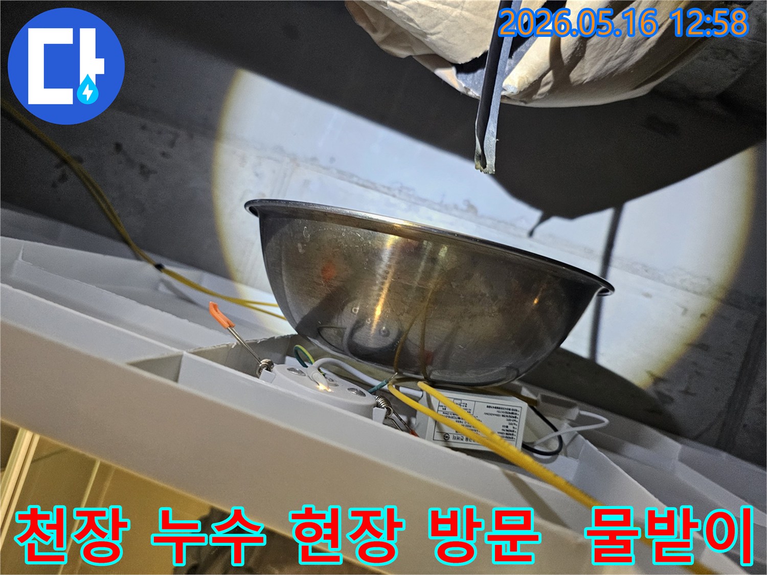 천장에서 물이 새는 것을-스테인리스 그릇으로-받아내며-전기 배선과-조명 장치 주변의-안전 상태를-점검하는 모습