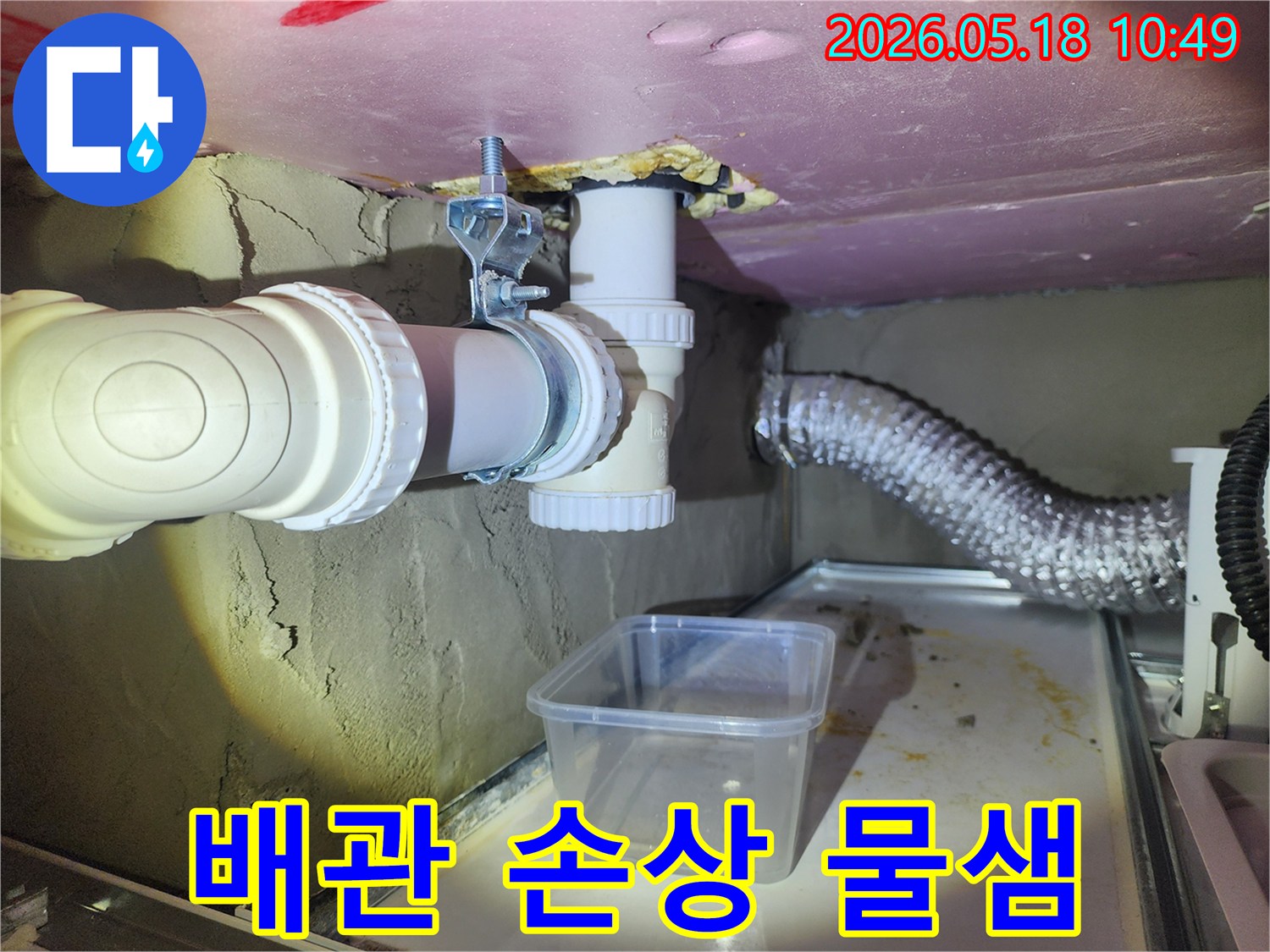 이 이미지는 손상된 배관에서 물이 새어 나와-임시 용기에 받아지고 있는 현장으로-신속한 조치가 필요함을 나타냅니다