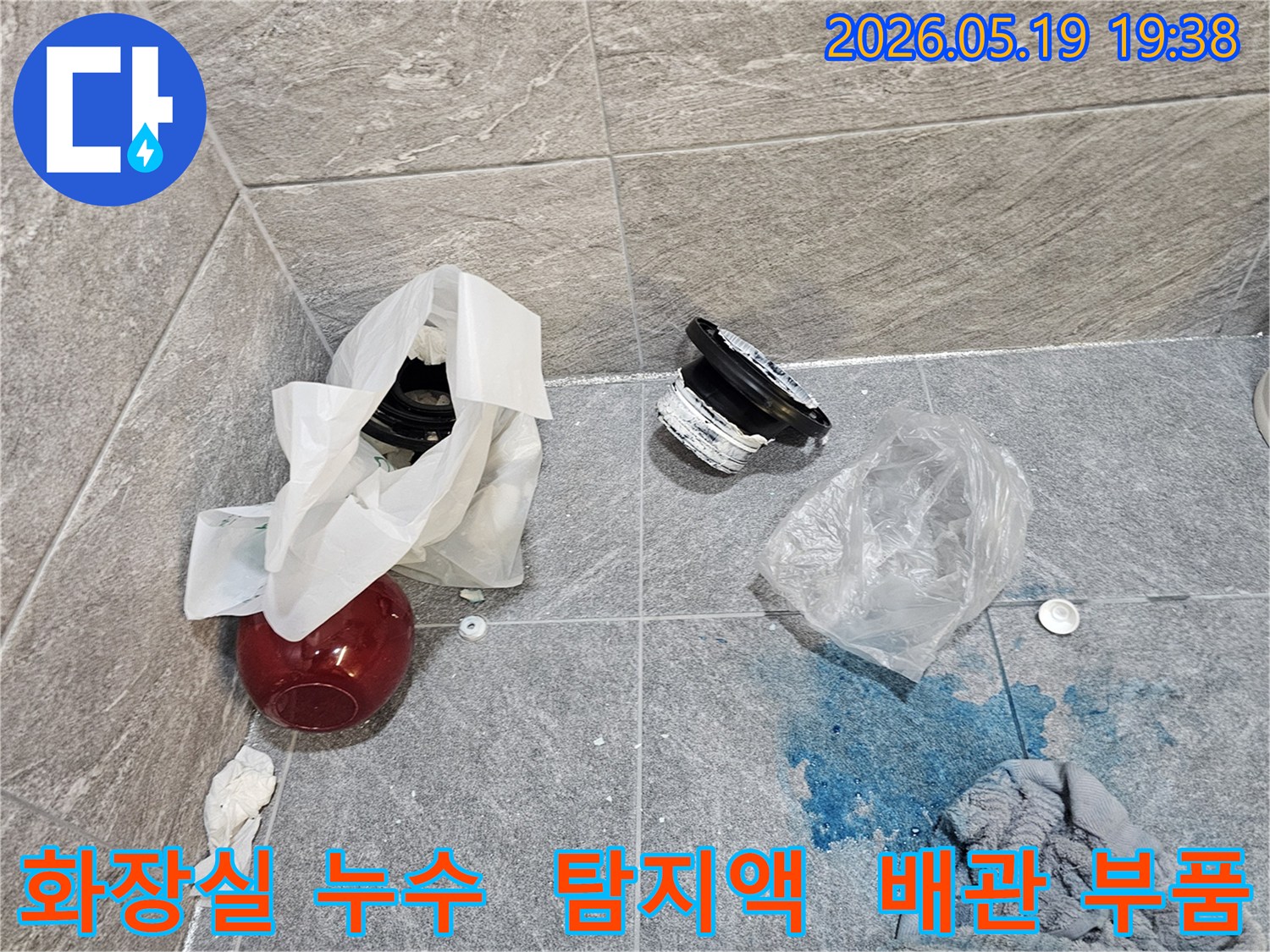 화장실 누수 탐지 현장에서-파란색 탐지액이 누수 지점을 가리키고-주변에는 손상된 배관 부품들이 놓여 있습니다