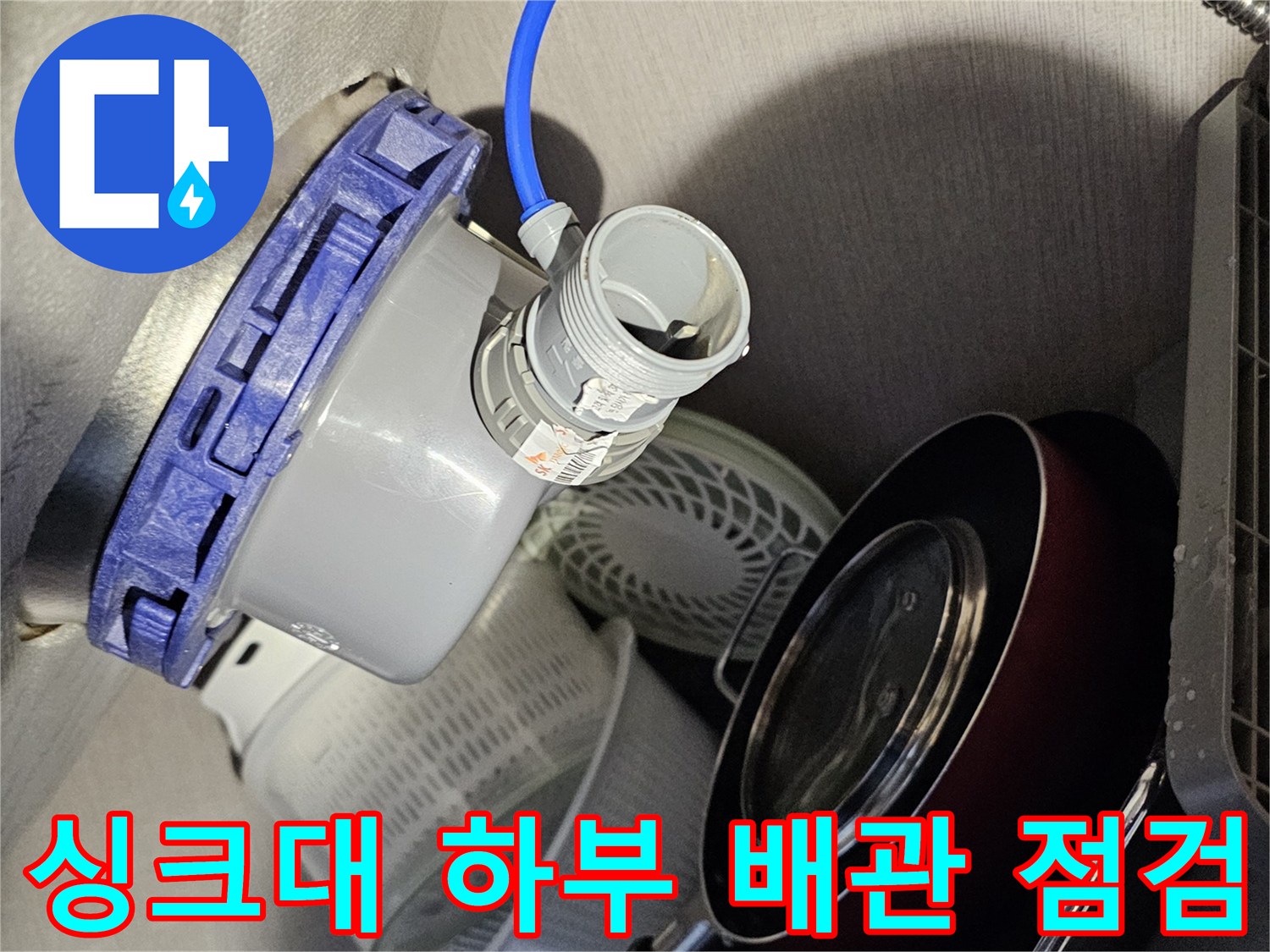 싱크대 하부장 내부의 파란색 호스와 배관 연결 부위 점검 모습