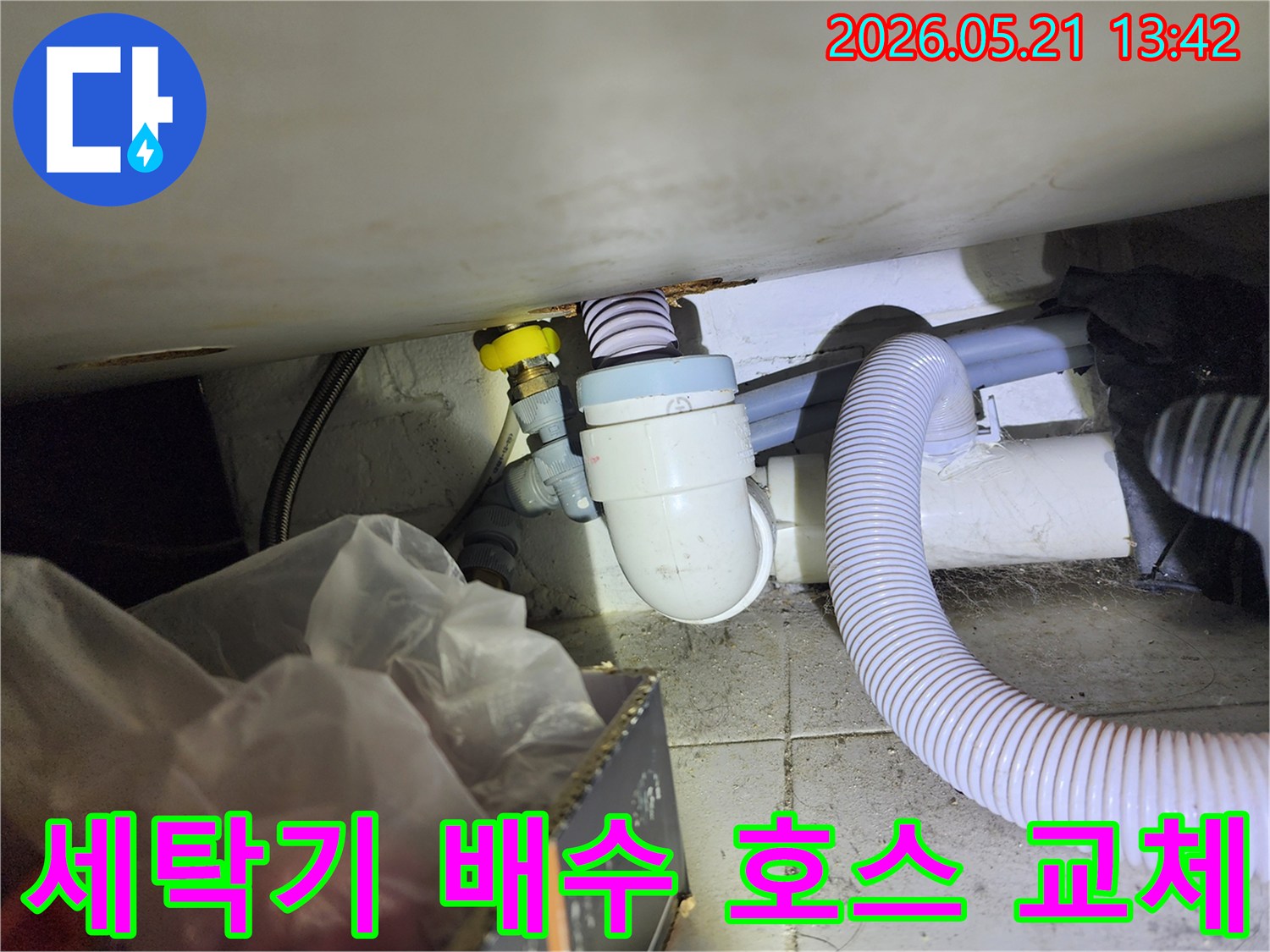 손상된 세탁기 배수 호스를 새것으로 교체하고-하수구에 단단히 연결하는 작업 현장입니다.