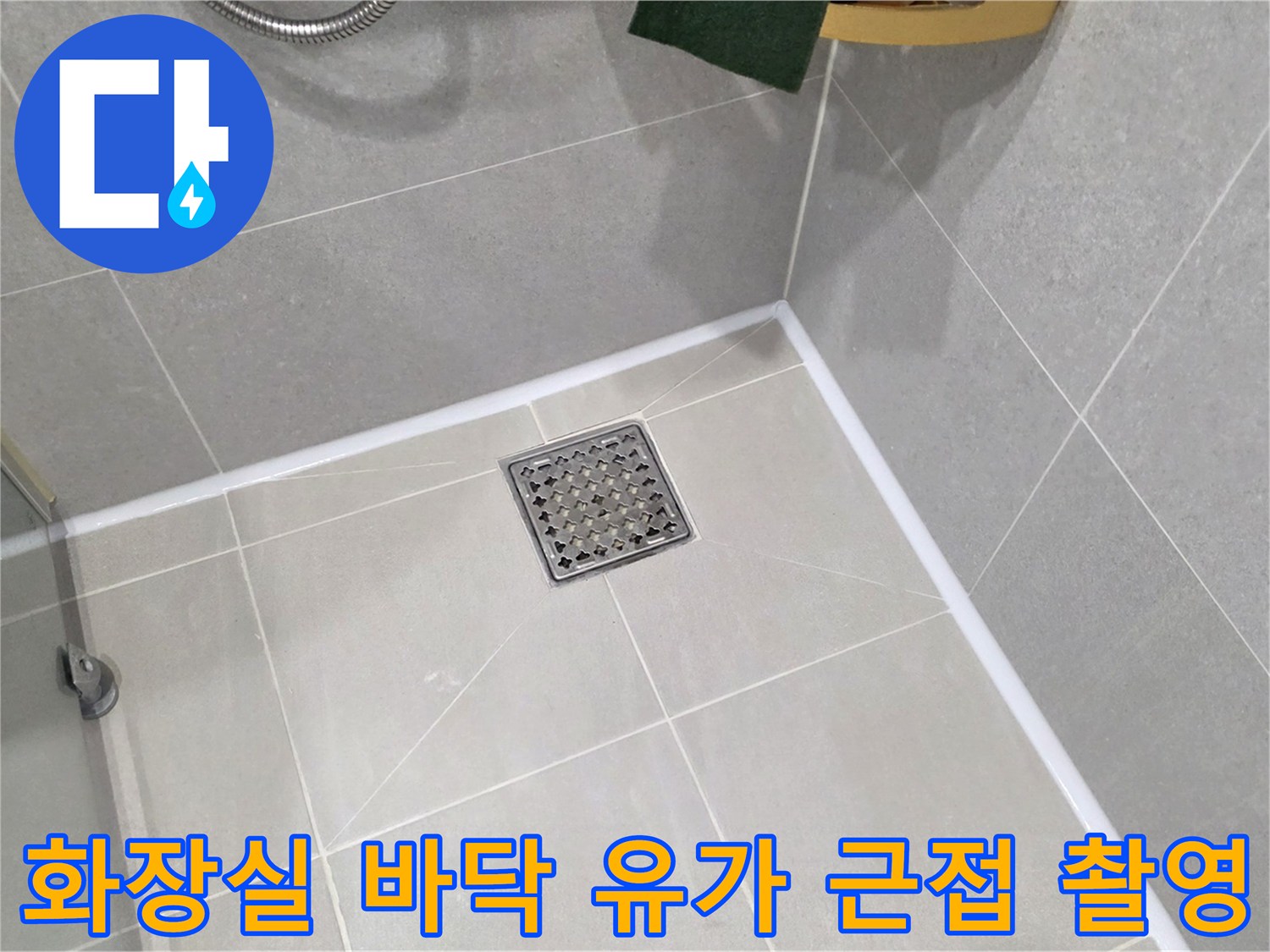 회색 욕실 타일 중앙에 위치한 금속 재질의 배수구 덮개