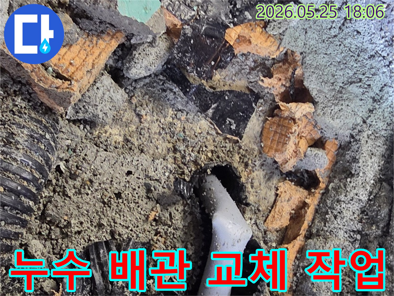 파쇄된 바닥 아래에서 드러난 젖은 배관과 주변의 흙-콘크리트 조각들은-누수 수리를 위한 배관 교체 작업을 보여줍니다.