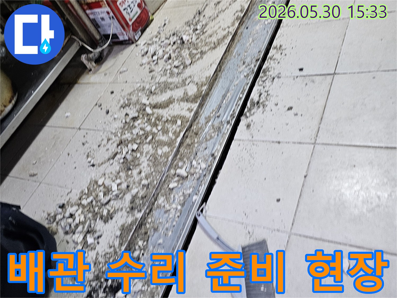 누수 공사 현장에서-바닥 타일 파쇄 후-발생한 잔해물과-청소 도구가-함께 보이는-작업 진행 모습입니다.