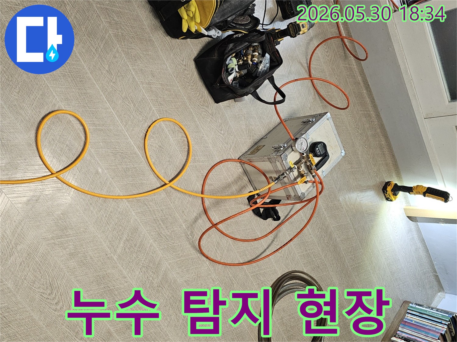 실내 바닥에 설치된 누수 탐지 장비와-다양한 연결 호스-그리고 작업 도구들이-누수 진단을 위해 준비된 장면입니다.