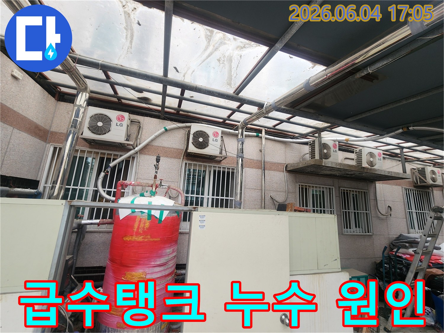 이 사진은 주택 외부에 설치된-빨간색 대형 급수탱크와-그 주변의 배관들을 보여줍니다