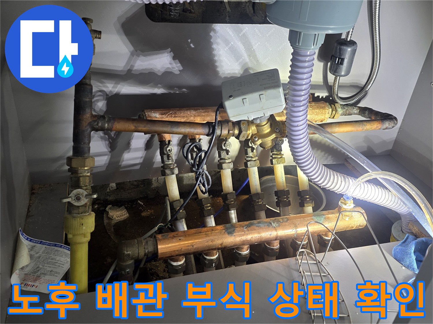 싱크대 하부장 내부의 노후된 보일러 분배기와 연결된 금속 배관들