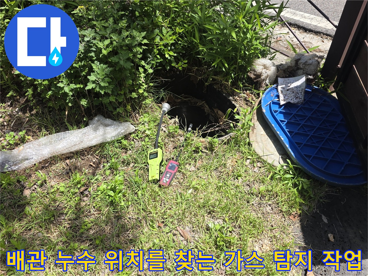풀숲 사이 맨홀 주변에서 가스 탐지기를 사용하여 배관의 파손 부위를 추적하는 장면입니다.