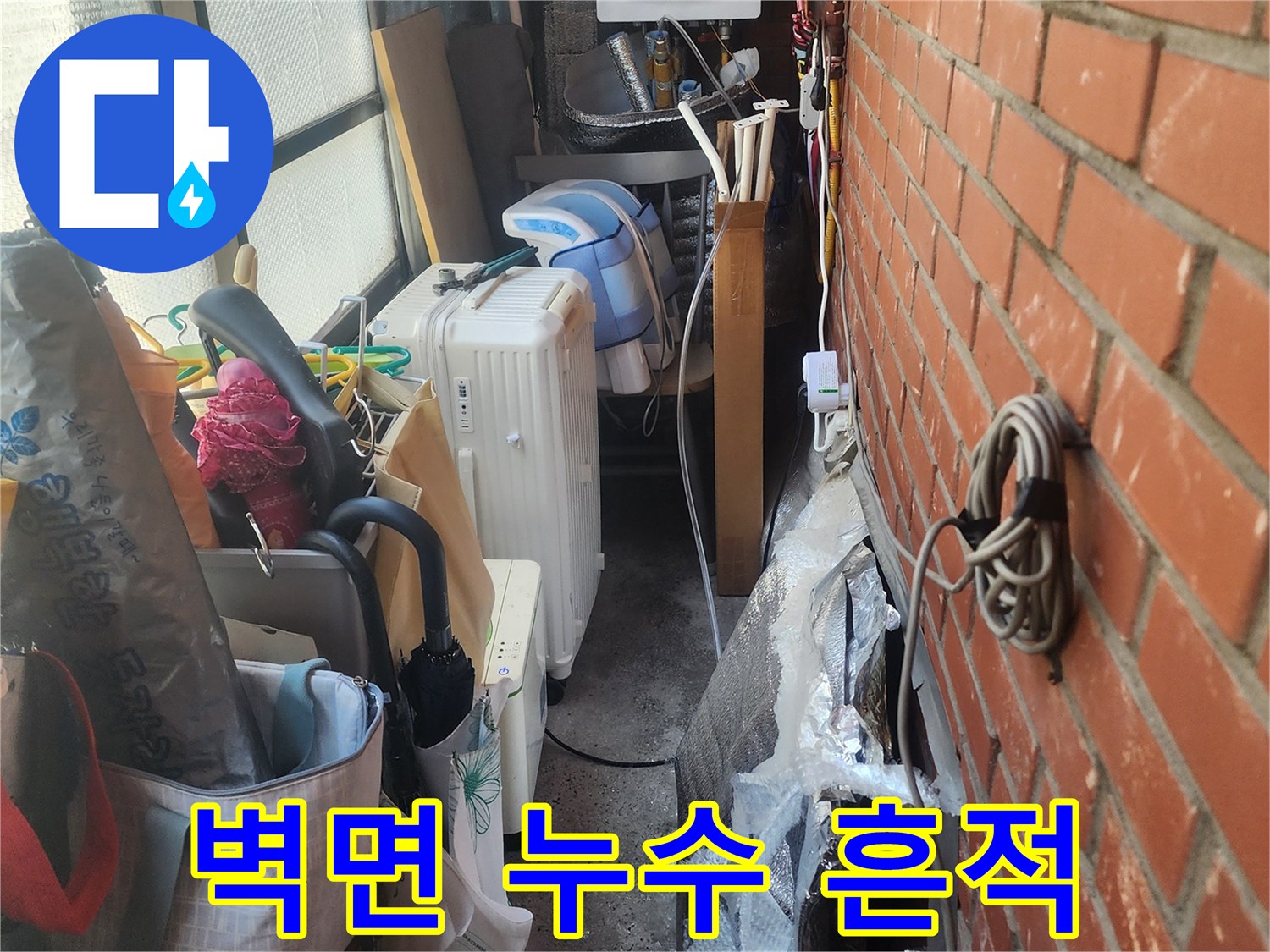 벽돌-벽-아래-복잡하게-얽힌-배관과-생활-용품들-사이에서-발견된-누수-흔적을-보여주는-사진