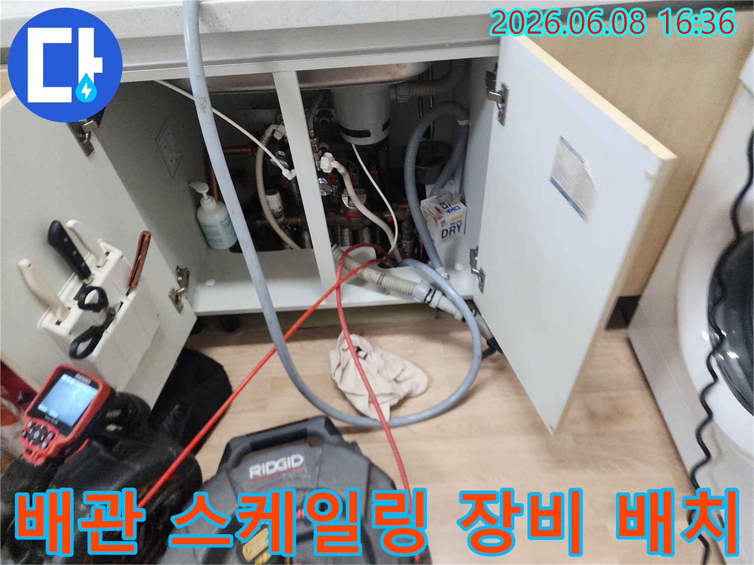싱크대 하부 배관 사이로 연결된 붉은색 케이블과 전문 스케일링 기계입니다.