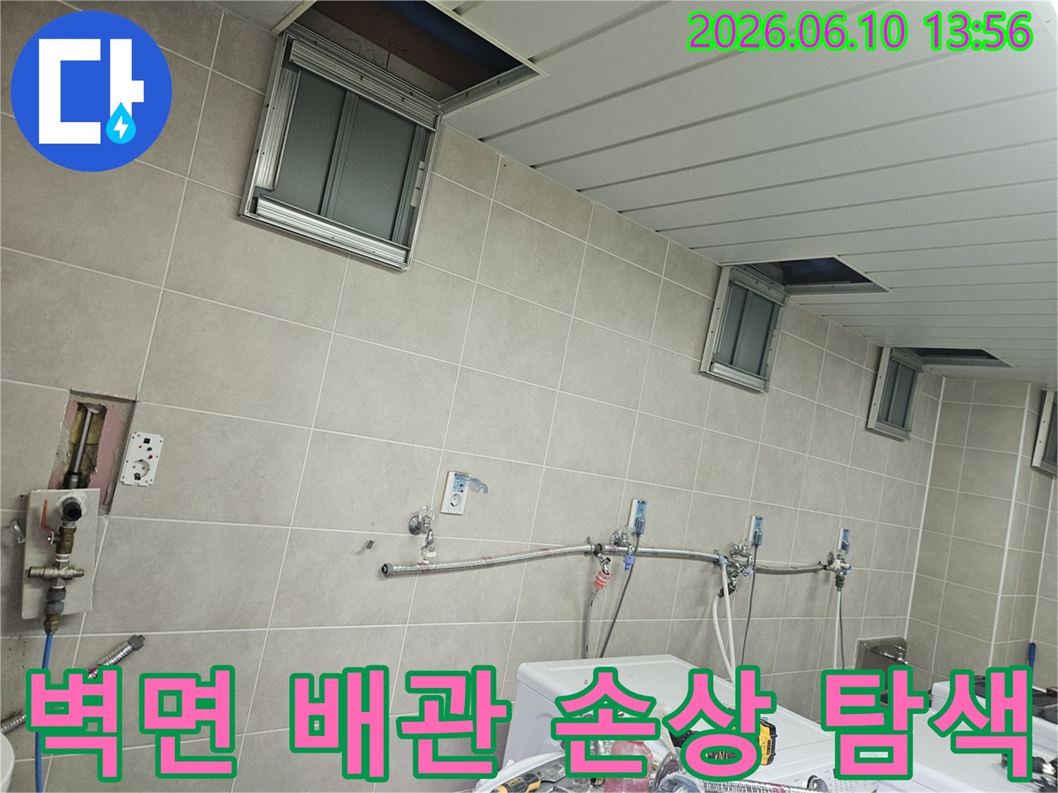 세탁실 벽면에 노출된 수도 배관과-그 주변의 숨겨진 배관 손상 여부를-면밀히 탐색하는 모습