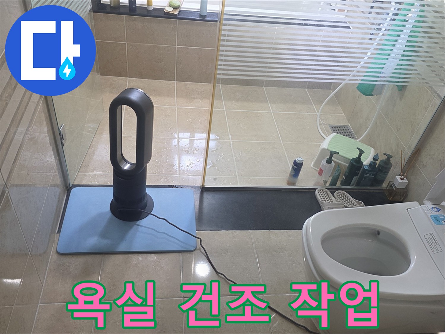 화장실 바닥 타일 위에서 작동 중인 공기 순환 장치와 변기 주변 모습