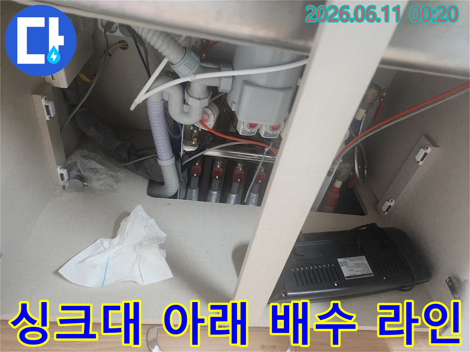싱크대 하부장 내부의 복잡한 분기 배관과 호스 연결 모습입니다.