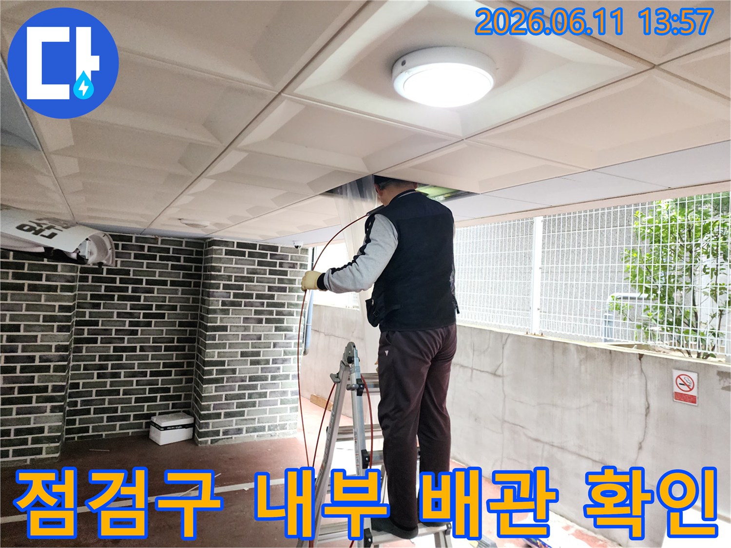 사다리에 올라가 천장 점검구로-배관의 막힘 지점을 찾기 위해-내시경 장비를 조작하는 모습입니다.