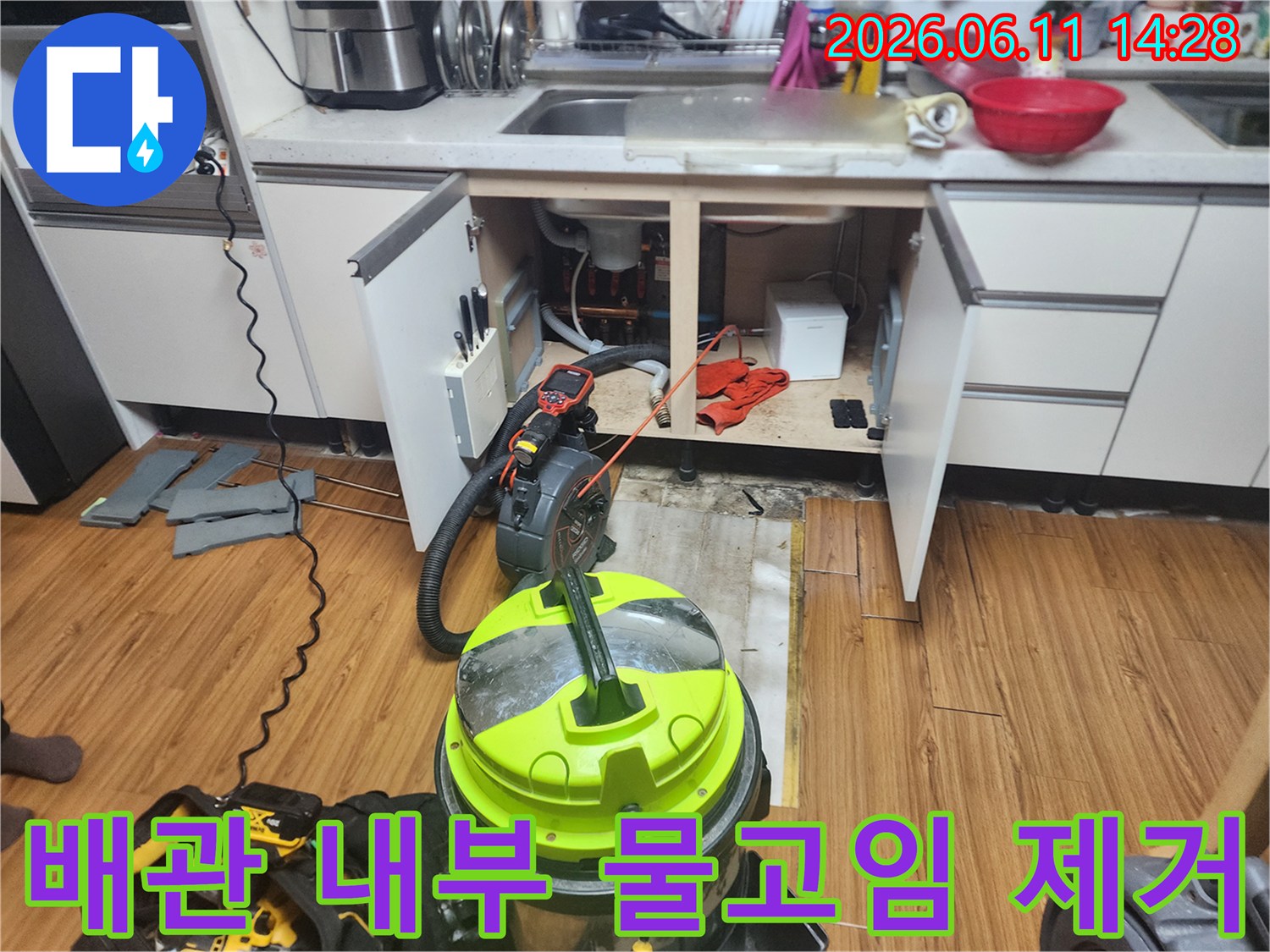 노란색 석션 장비를 사용하여 싱크대 하부 배관의 고인 물을 흡입하고 있습니다.