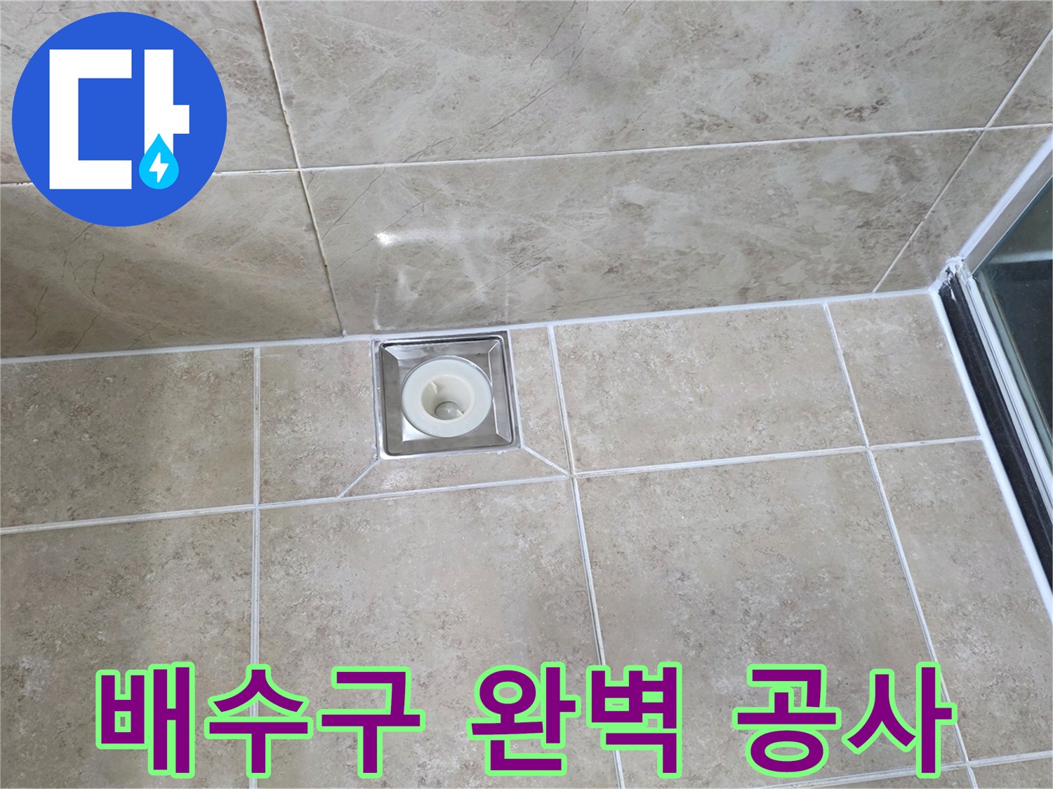 베이지색 타일 바닥에 설치된-금속 사각 배수구의 모습으로-주변 타일과 줄눈의 마감 상태를 보여줍니다