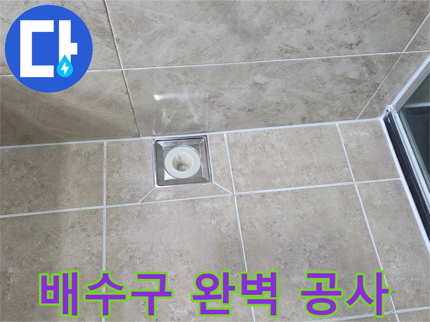 베이지색 타일 바닥에 설치된-금속 사각 배수구의 모습으로-주변 타일과 줄눈의 마감 상태를 보여줍니다