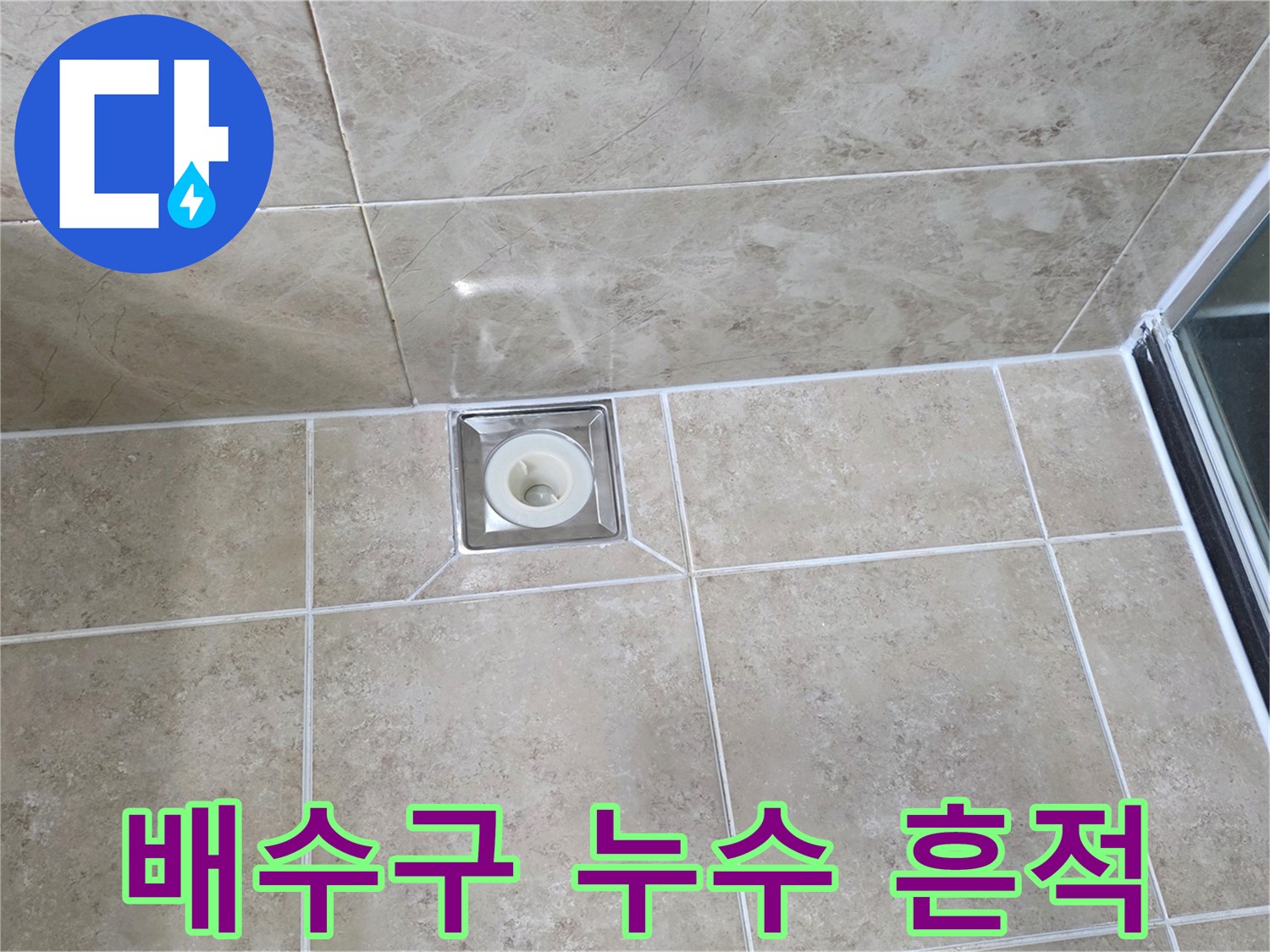 베이지색 타일 바닥에 설치된-사각형 금속 배수구의 모습으로-주변 타일과 줄눈의 상태를 면밀히 관찰하는 이미지입니다