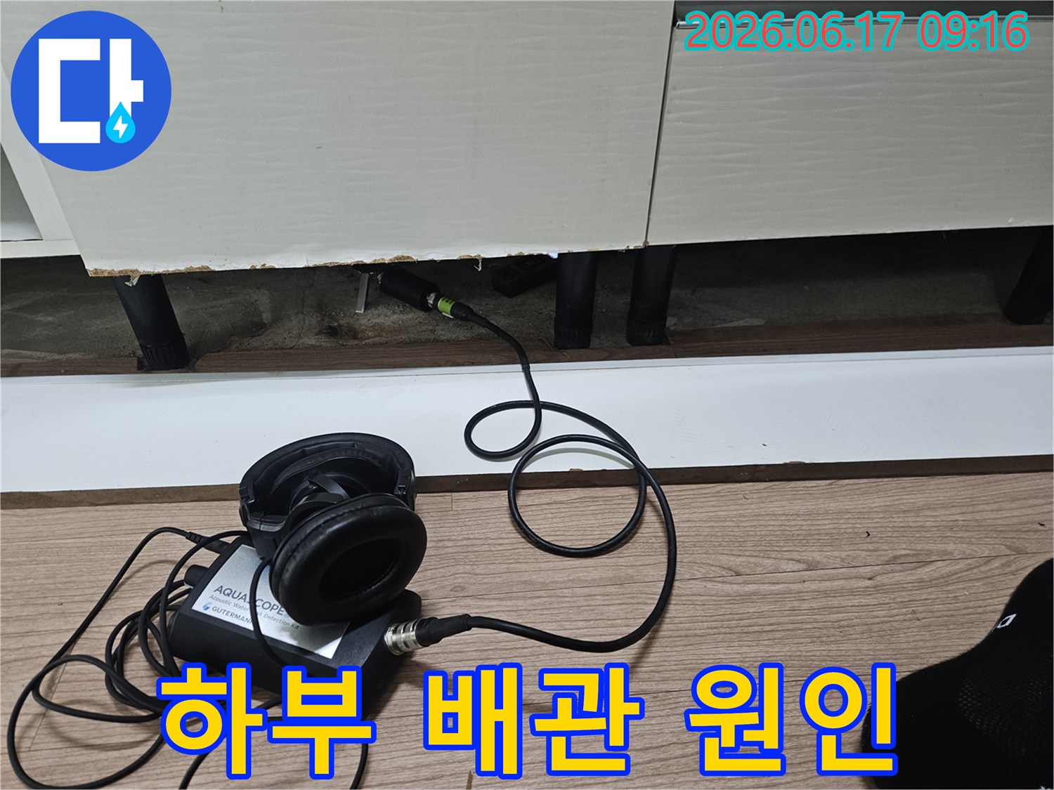 누수 탐지 장비의 본체와 헤드폰이-싱크대 하부장 아래-누수 센서와 연결되어 있는 모습