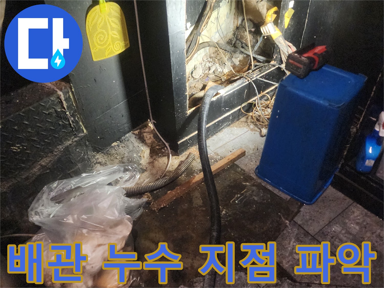 어둡고 협소한 공간에서 복잡하게 얽힌 배관과 전선-그리고 물이 고여있는 바닥을 보여주며 누수 지점을 파악하는 현장