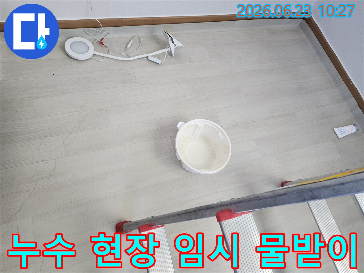 누수로 인해 바닥에 물이 떨어지는 것을 임시로 받는 그릇과-누수 지점 확인을 위한 사다리-작업용 조명 장비가 바닥에 놓여 있는-누수 공사 전 현장 모습입니다