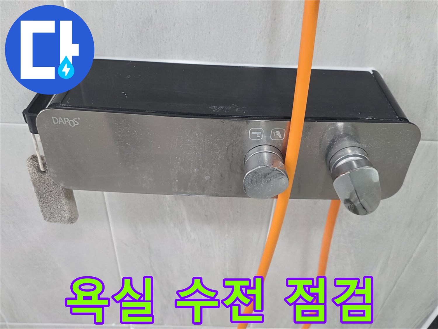 욕실 벽면에 설치된 스테인리스 수전과 주황색 호스 모습