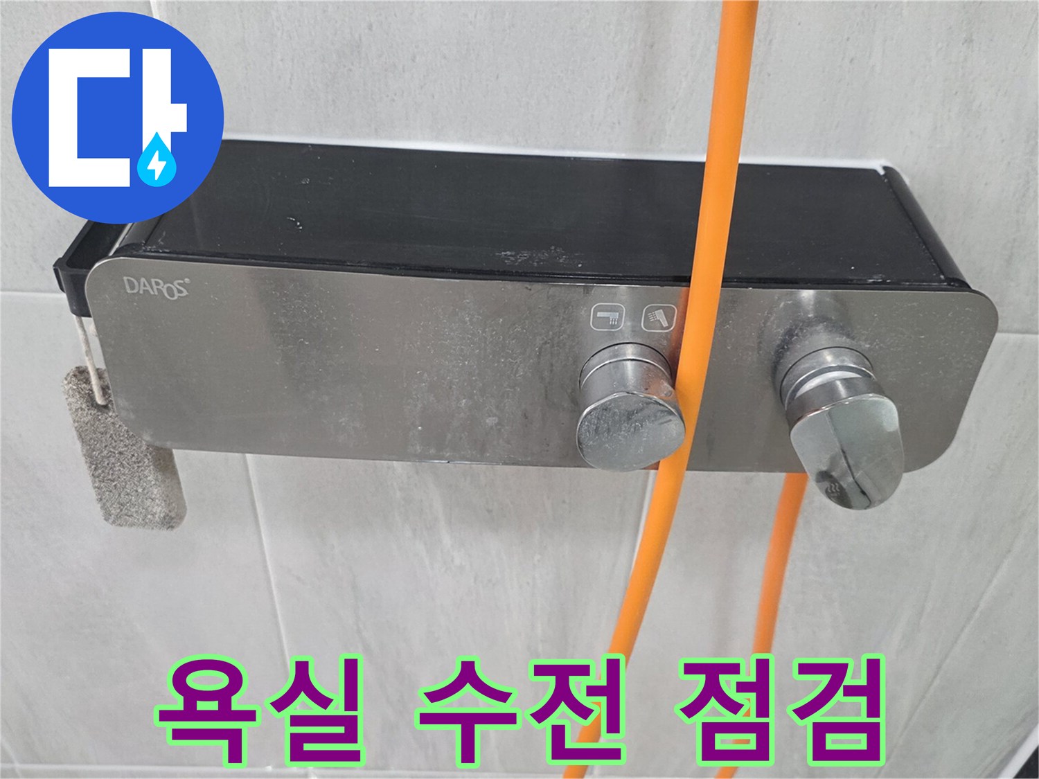 욕실 벽면에 설치된 은색 수전과 주황색 호스 모습