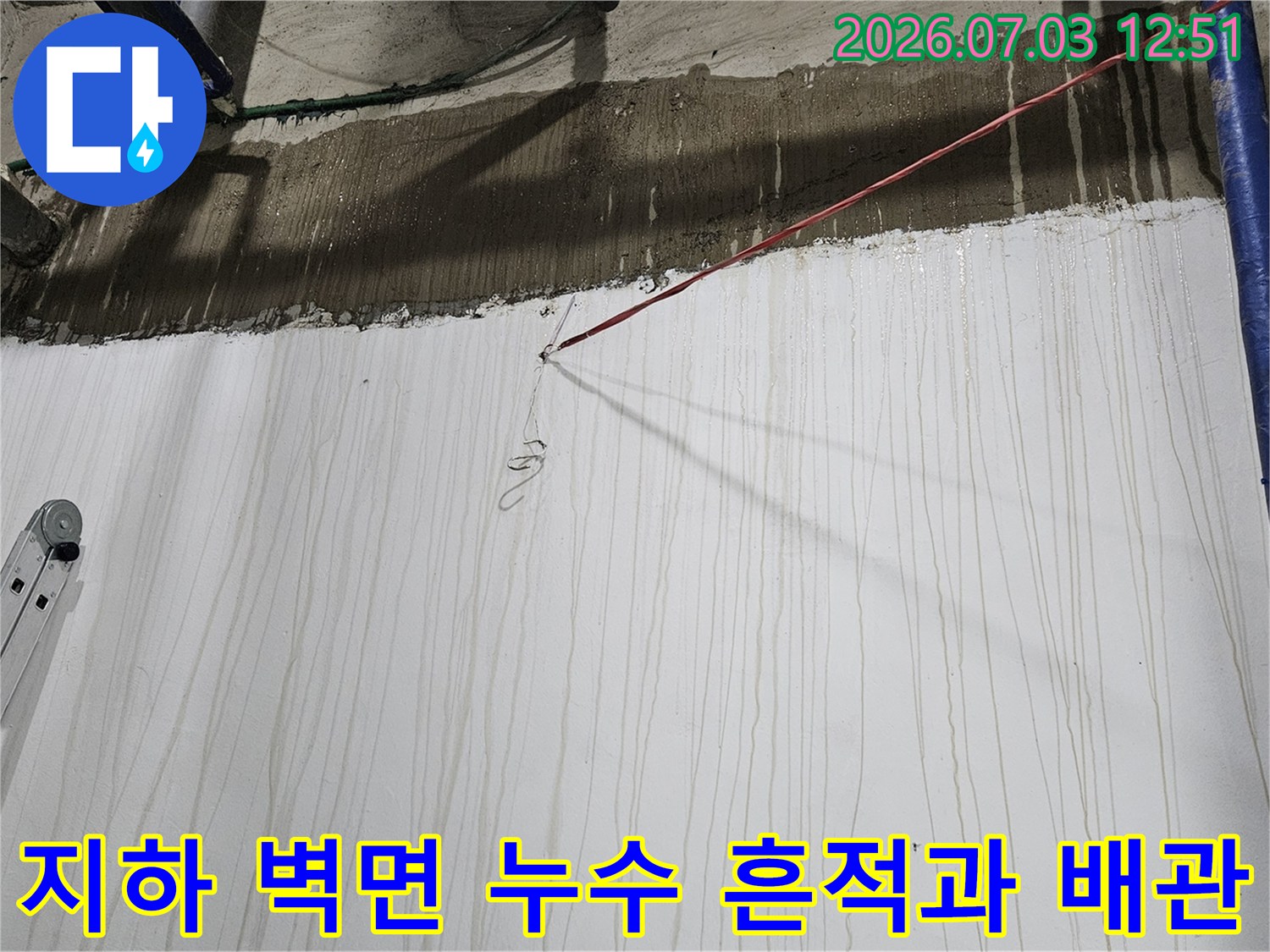 지하 공간의 하얀색 벽면에 물이 흘러내린 자국이 있고 파란색 보온재가 감싸진 배관이 설치된 모습