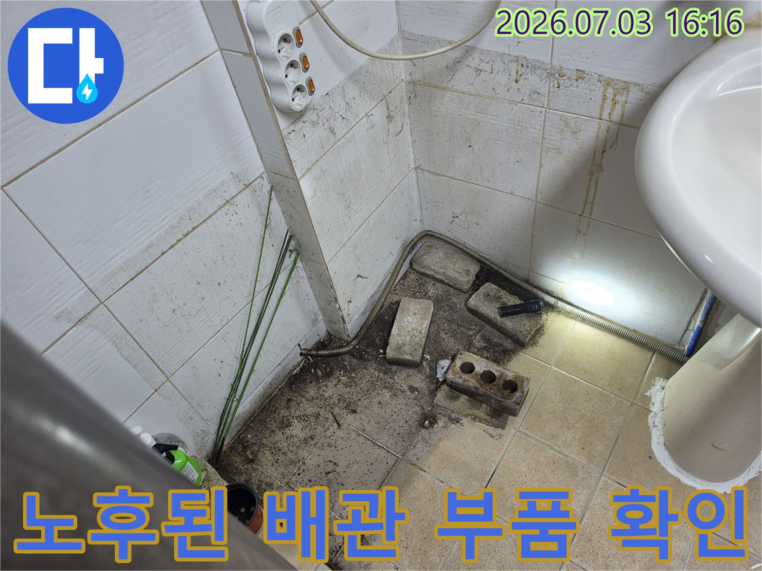 오염된 타일 위로 노출된 세면대 연결용 하부 배관들