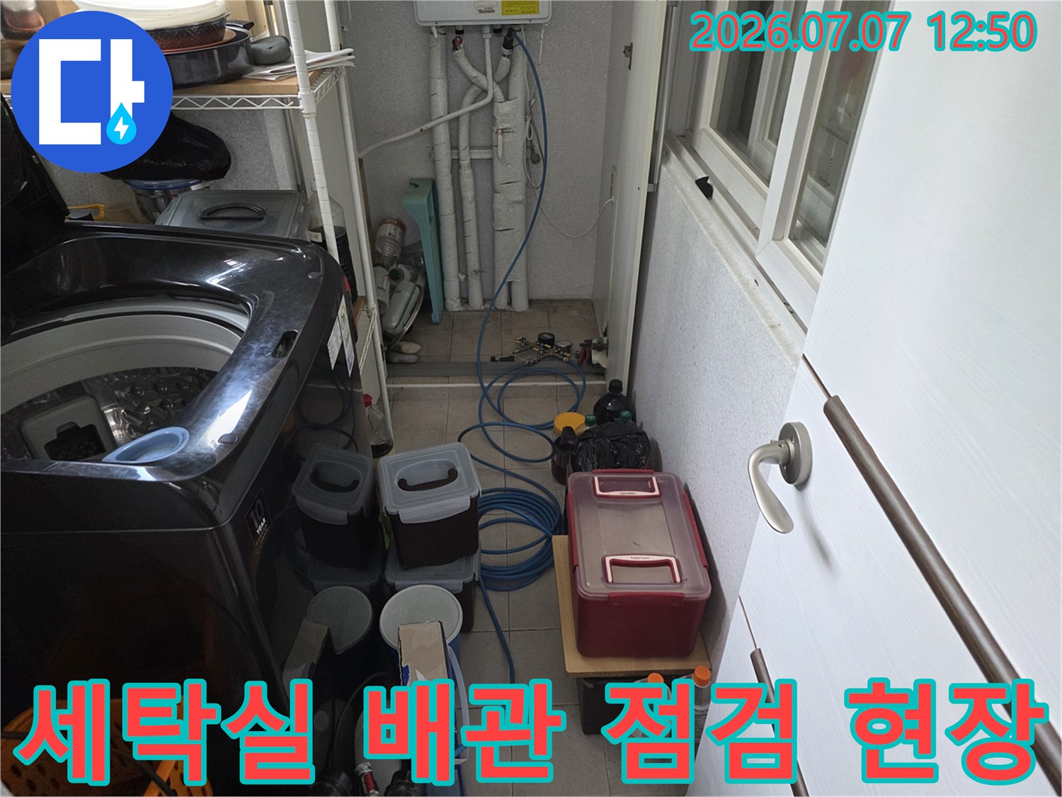 세탁실 바닥에 놓인 각종 장비와 노출된 수도 배관 및 호스 연결 부위