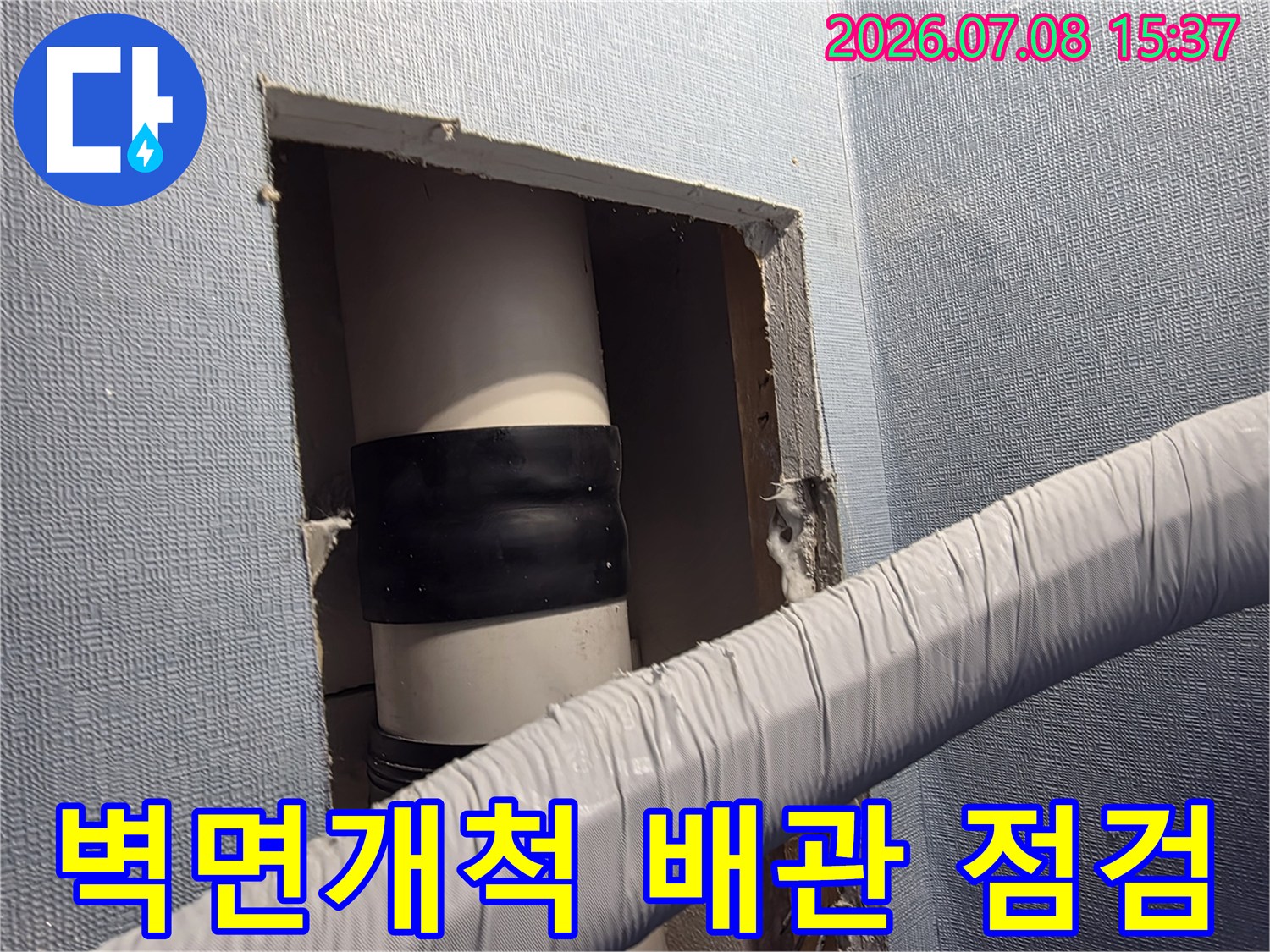 벽체를 절개하여 노출된 에어컨 배수관과 검은색 테이핑 처리된 연결 부위의 모습