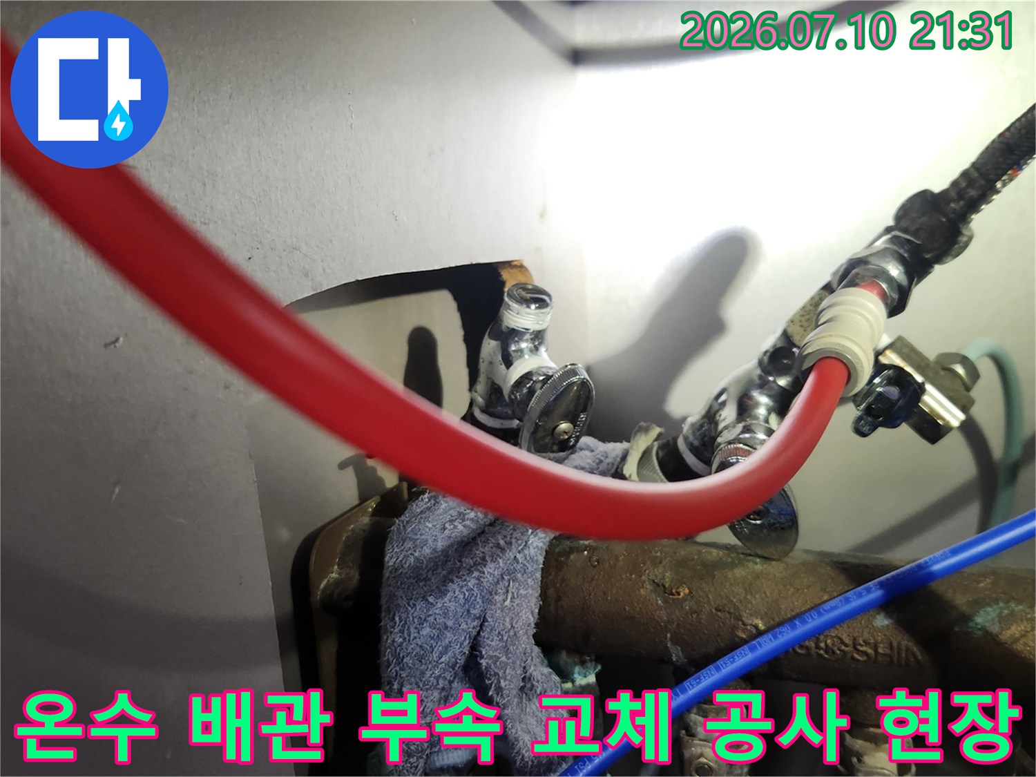싱크대 밑에 위치한 붉은색 온수 호스와 금속 배관 연결부 보수 모습