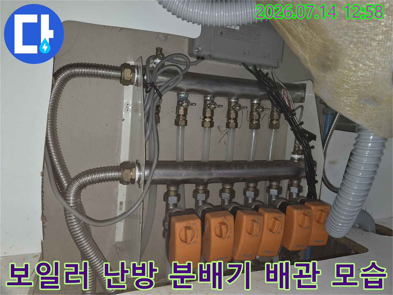 벽면에 설치된 금속 재질의 보일러 분배기와 주황색 밸브 손잡이들-난방 배관 시스템