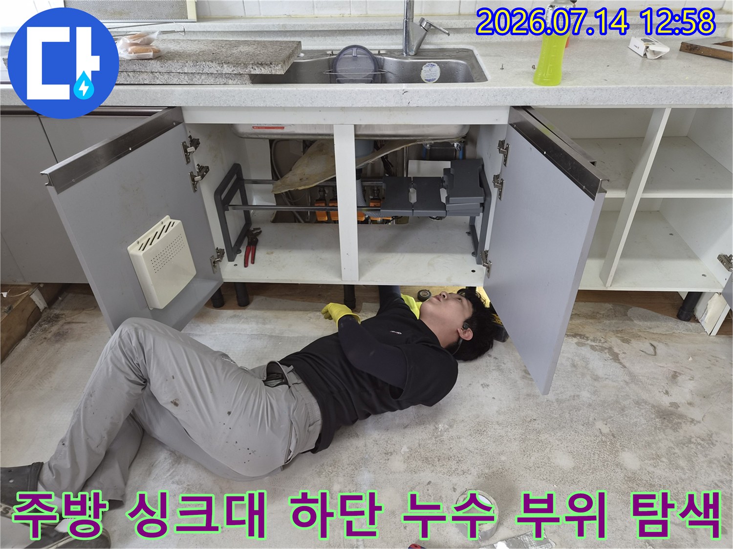 작업자가 싱크대 하부에 누워 배관 연결 상태를 세밀하게 관찰하는 모습
