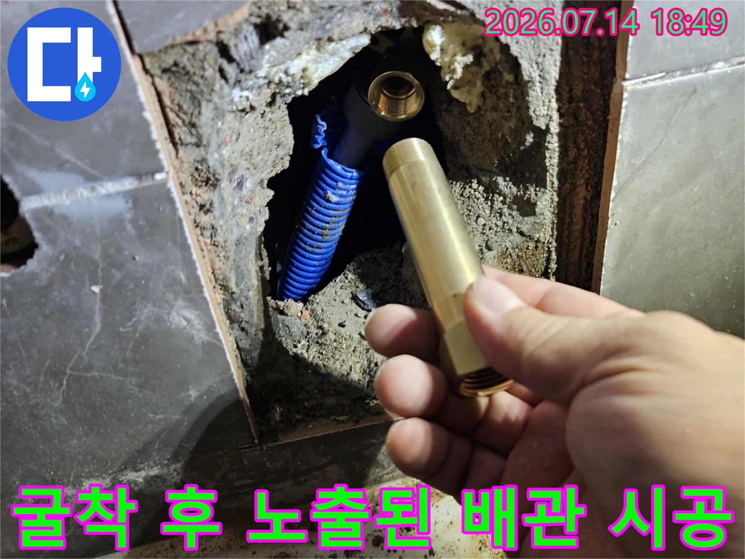 손에 든 금속 수전 부품과 파란색 주름 배관이 대비되는 작업 현장 모습