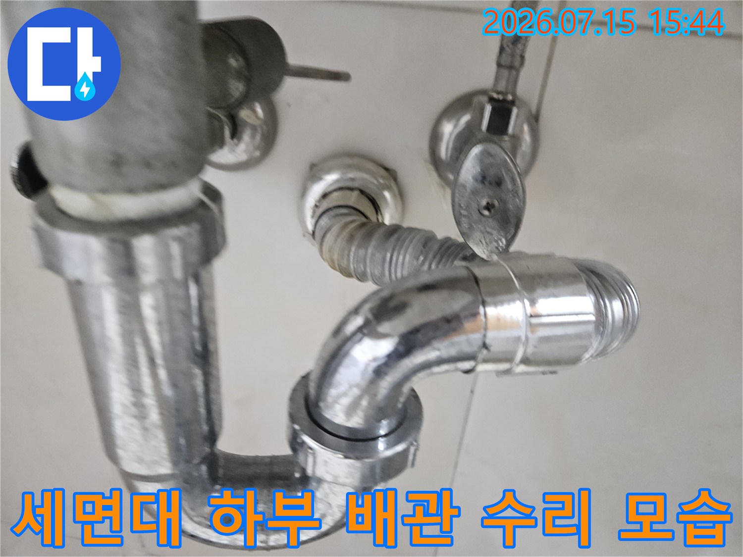 세면대 아래 위치한 스테인리스 소재의 배관 연결 부위 수리 장면