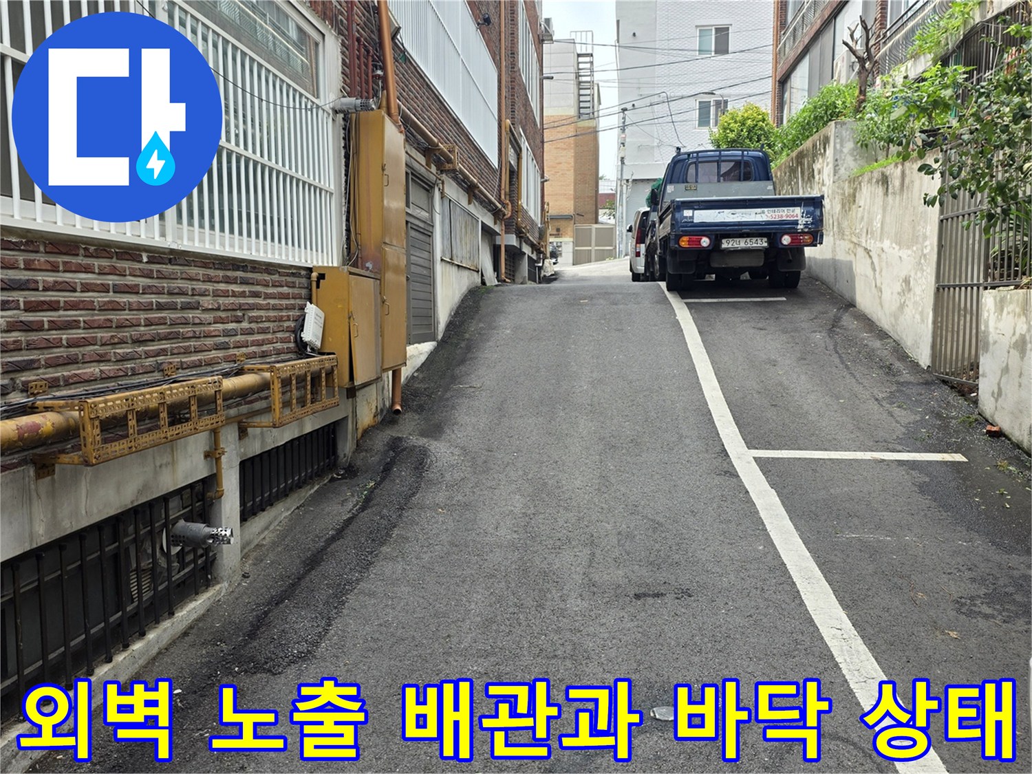 건물 벽면의 노출된 배관과 아스팔트 도로의 연결 부위