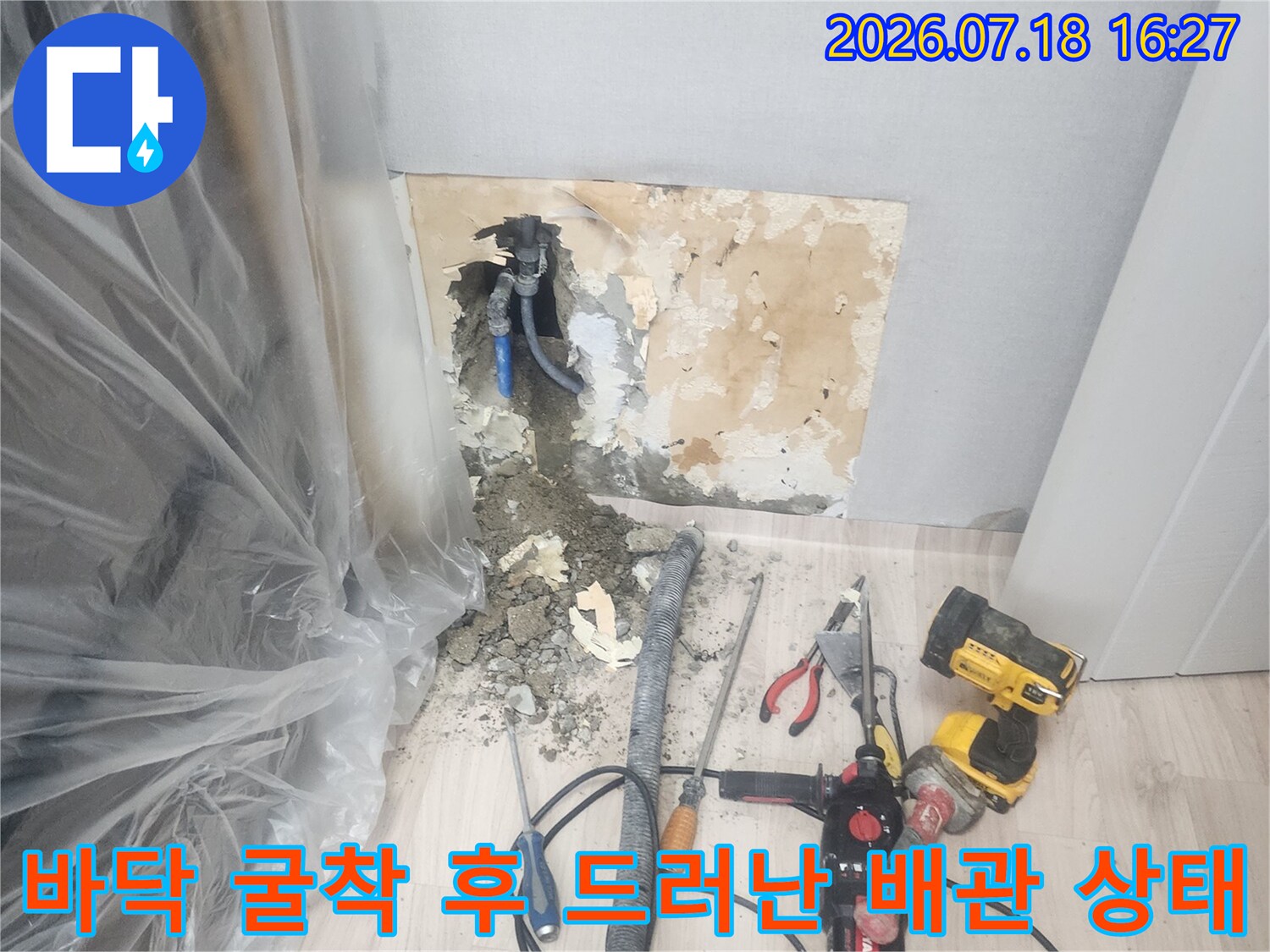 바닥 일부를 제거하고 드러낸 파란색 배관-주변에 전동드릴과 집진 호스가 연결됨