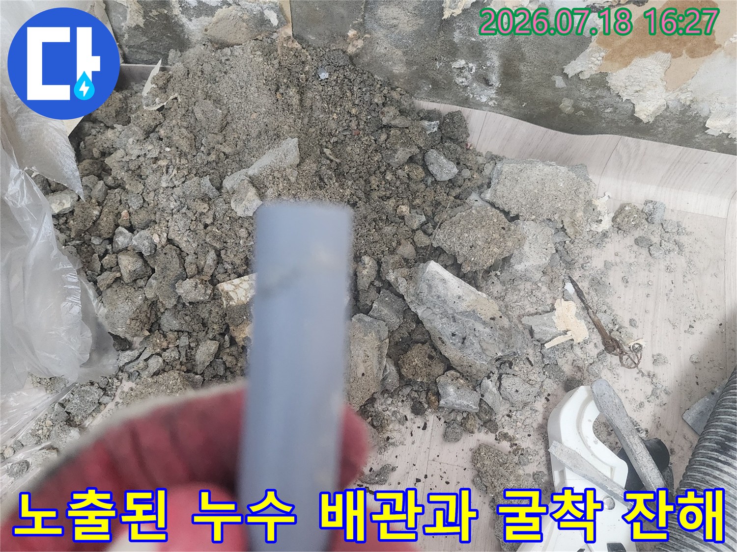 작업자가 장갑을 끼고 손상된 회색 수도 배관 부위를 가리키고 있는 모습