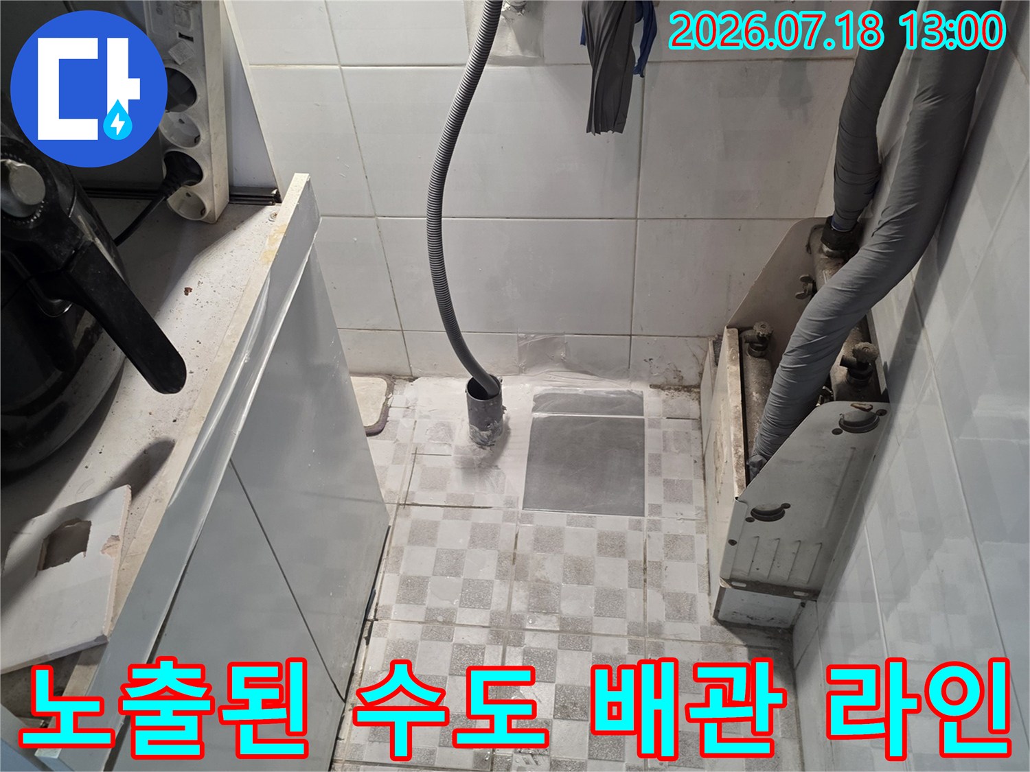 벽면에 고정된 회색 보온재 관과 노란색 호스 및 주변 타일 모습