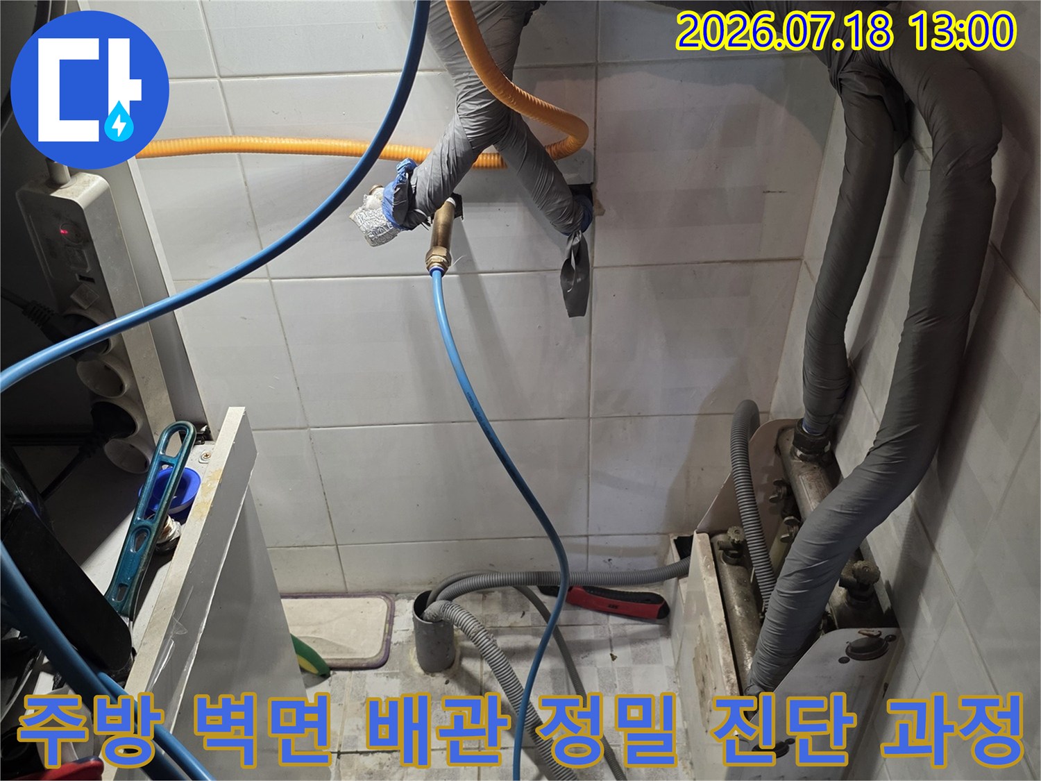 흰색 타일 벽면에 설치된 보온재 처리된 배관과 파란색 및 노란색 탐지 호스가 연결된 모습