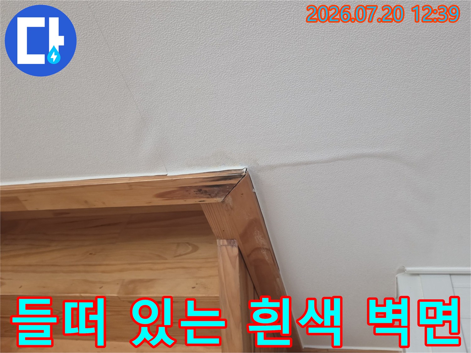 나무 선반 위쪽의 벽지가 누수로 인해 표면이 고르지 않고 부푼 모습