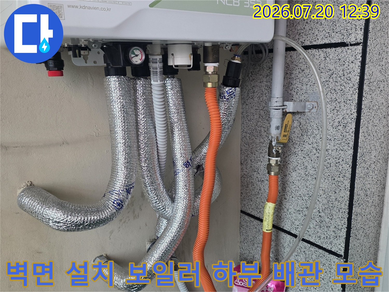 흰색 가스보일러 아래로 연결된 은색 단열재 처리 배관과 주황색 보호관들의 배치