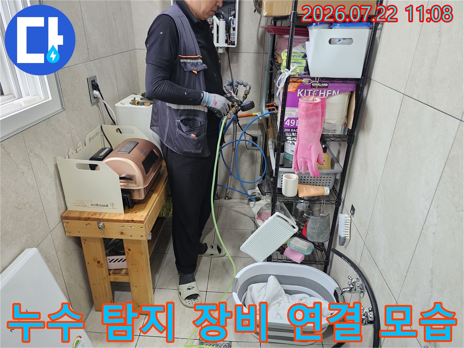 작업자가 파란색과 노란색 호스가 연결된 전문 누수 탐지 장비를 이용해 배관 상태를 점검하고 있는 모습