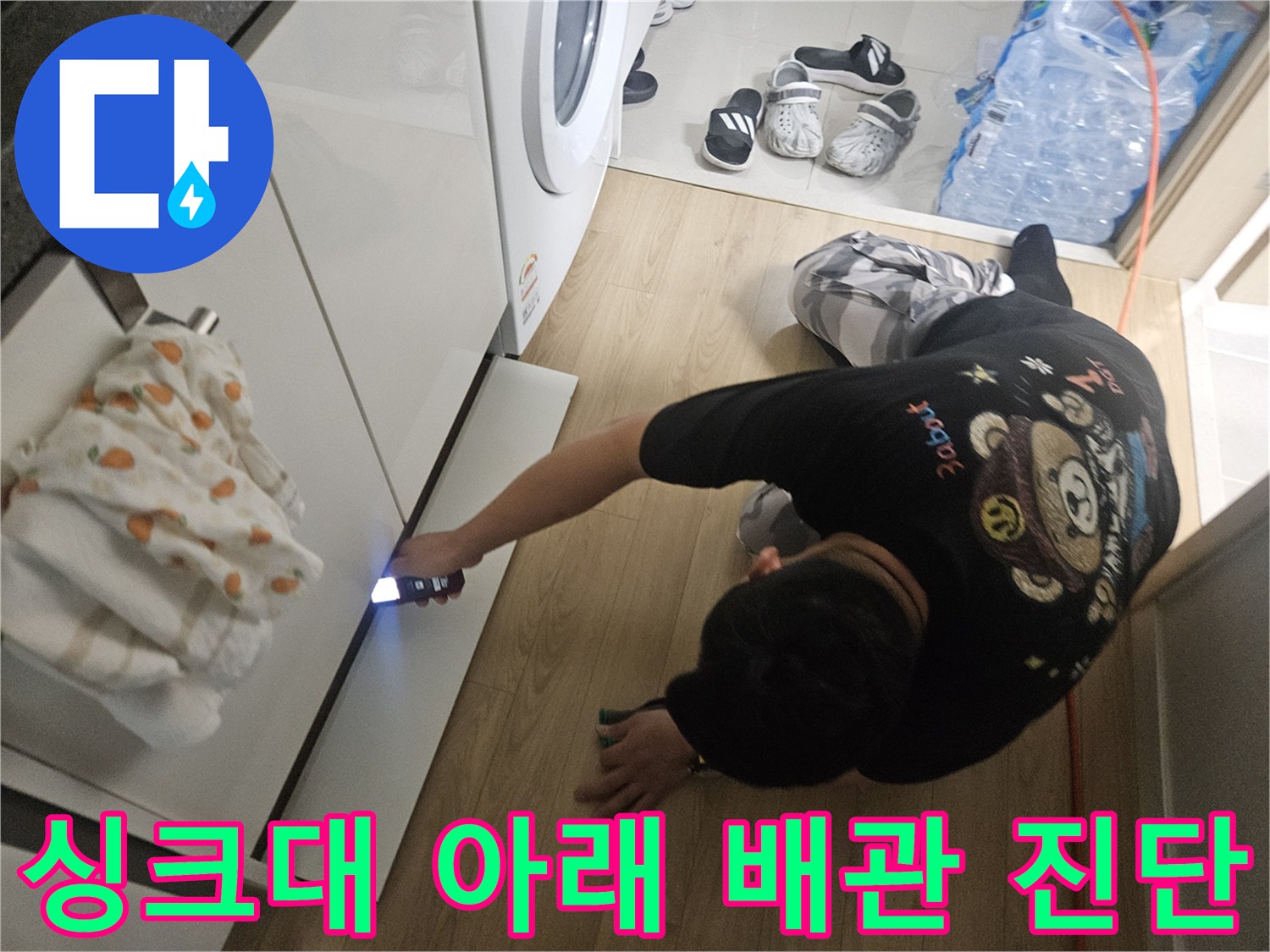 어두운 싱크대 밑 공간에 손전등을 비추며 배관을 살피는 작업자