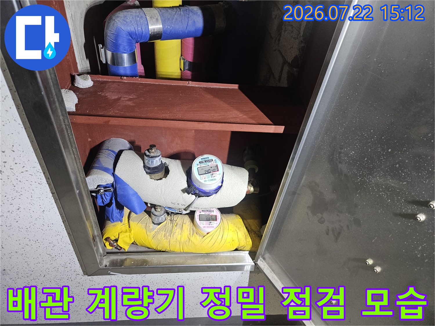 파란색-노란색 보온재로 감싸진 배관과 상단에 설치된 디지털 계량기의 모습