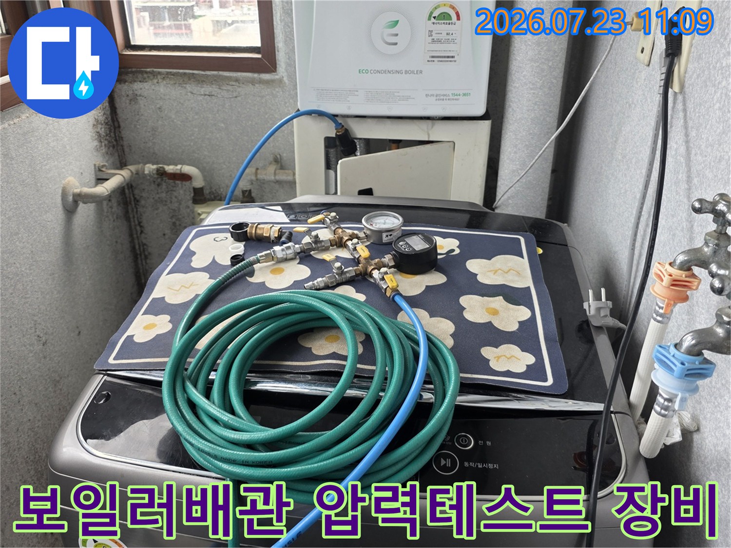 세탁기 위에 놓인 꽃무늬 매트와 디지털 압력계-가스 탐지용 호스가 연결된 모습